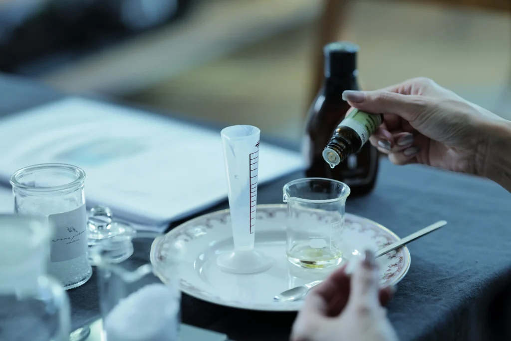 ビーカーに精油をおとしている様子。机の上には他にもガラスの瓶やオイルなど