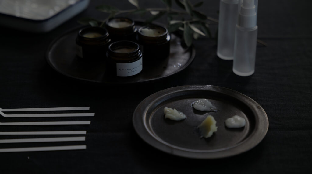 机の上にムエット、ガラスの容器、スプレーボトル。お皿の上にはシアバターがのっている様子